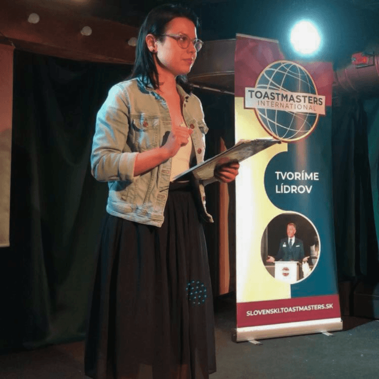 Moderátorka vedie klubové stretnutie Toastmasters s agendou v ruke
