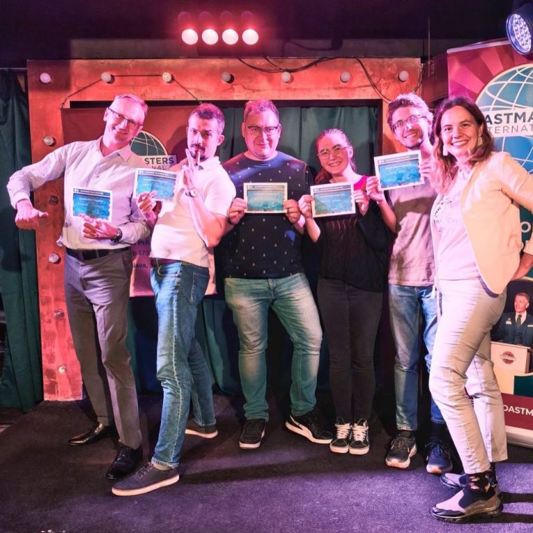 Šesť usmiatych členov Toastmasters s diplomami na pódiu po stretnutí klubu – priateľská atmosféra, v ktorej chyba nič nestojí